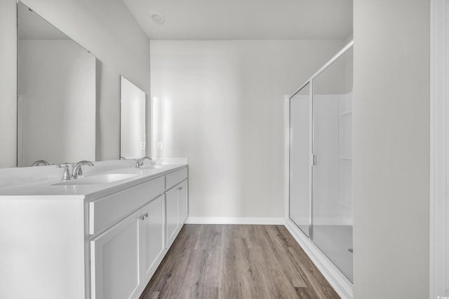 bathroom featuring a sink, double vanity, a stall shower, and wood finished floors