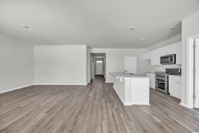 kitchen with stainless steel appliances, white cabinets, open floor plan, light stone countertops, and a center island with sink