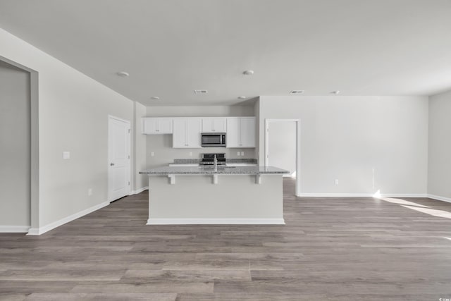 kitchen with a breakfast bar area, stainless steel appliances, stone countertops, white cabinets, and an island with sink