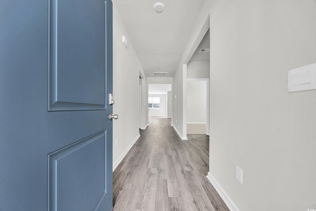 hall with light wood finished floors, visible vents, and baseboards