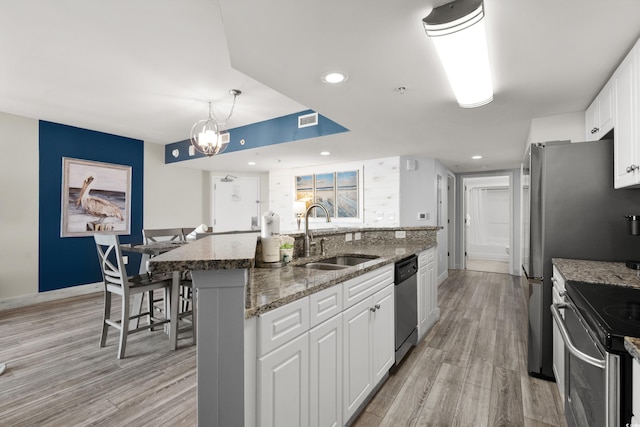 kitchen featuring sink, appliances with stainless steel finishes, white cabinetry, a center island with sink, and stone countertops