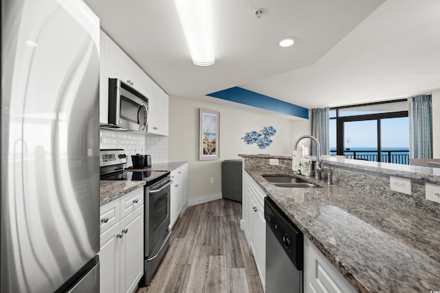 kitchen with stone counters, appliances with stainless steel finishes, white cabinetry, sink, and a water view