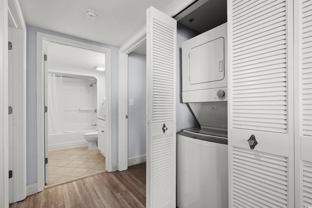 clothes washing area with hardwood / wood-style flooring and stacked washing maching and dryer