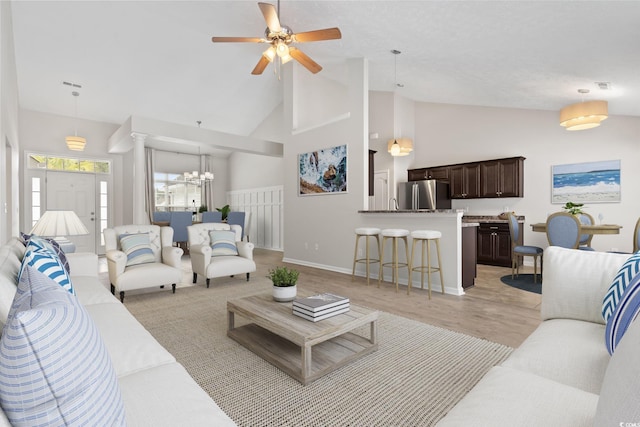 living room with high vaulted ceiling, ceiling fan with notable chandelier, and light hardwood / wood-style floors