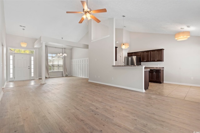 unfurnished living room featuring ceiling fan with notable chandelier, ornate columns, high vaulted ceiling, and light wood-type flooring