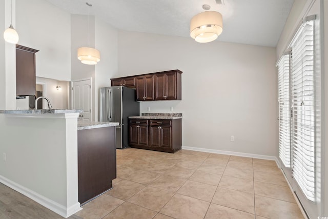 kitchen featuring dark brown cabinetry, light tile patterned floors, hanging light fixtures, and stainless steel refrigerator