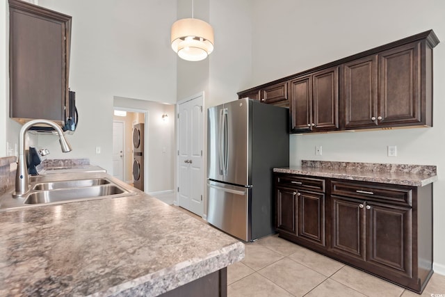 kitchen featuring dark brown cabinetry, sink, stainless steel fridge, and stacked washing maching and dryer