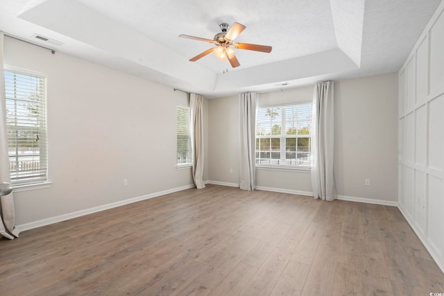 spare room with a raised ceiling, hardwood / wood-style flooring, a textured ceiling, and ceiling fan