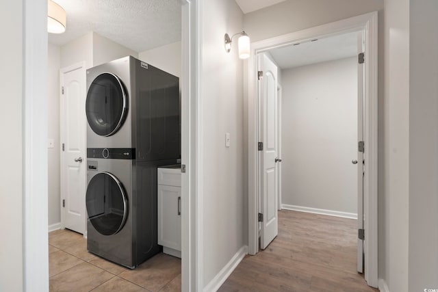 washroom featuring cabinets, stacked washing maching and dryer, light tile patterned floors, and a textured ceiling