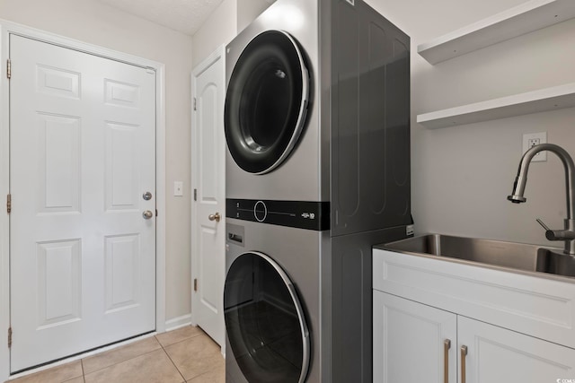 laundry room featuring stacked washer and dryer, light tile patterned floors, cabinets, and sink