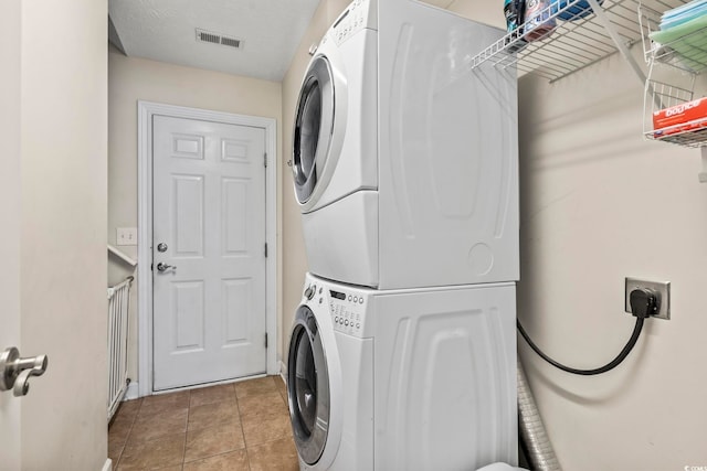 laundry room featuring light tile patterned floors, a textured ceiling, and stacked washing maching and dryer