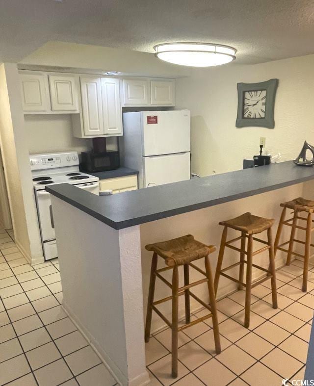 kitchen featuring white appliances, a kitchen bar, kitchen peninsula, and white cabinets