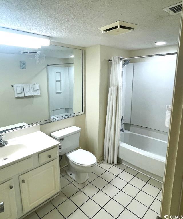 full bathroom with shower / tub combo with curtain, tile patterned flooring, vanity, toilet, and a textured ceiling