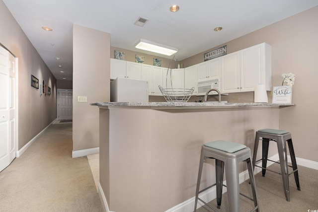 kitchen featuring white appliances, a breakfast bar, white cabinetry, light stone countertops, and kitchen peninsula