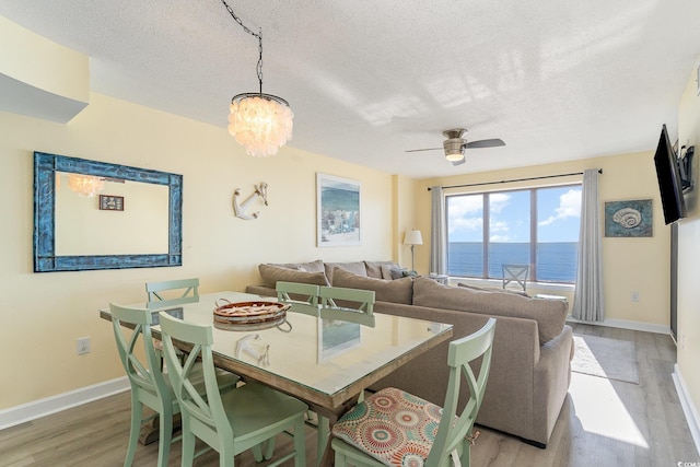 dining area with ceiling fan with notable chandelier, a textured ceiling, and light hardwood / wood-style floors