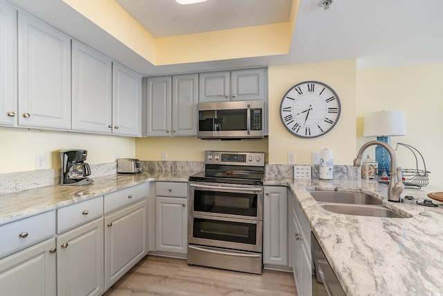 kitchen with appliances with stainless steel finishes, sink, gray cabinetry, light stone counters, and light hardwood / wood-style floors