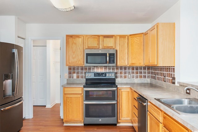 kitchen featuring appliances with stainless steel finishes, light brown cabinetry, tasteful backsplash, sink, and light wood-type flooring