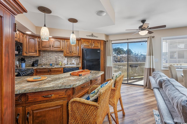 kitchen featuring sink, light stone counters, black appliances, light hardwood / wood-style flooring, and backsplash