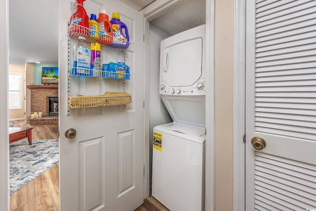 laundry area with hardwood / wood-style flooring, a fireplace, stacked washer and clothes dryer, and a textured ceiling