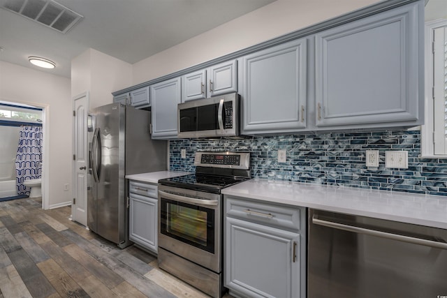 kitchen featuring gray cabinetry, backsplash, hardwood / wood-style flooring, and appliances with stainless steel finishes