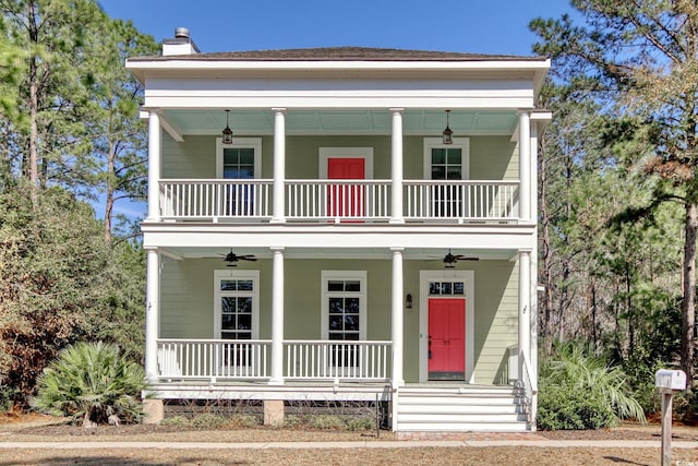 neoclassical home featuring a balcony, a ceiling fan, covered porch, and a chimney