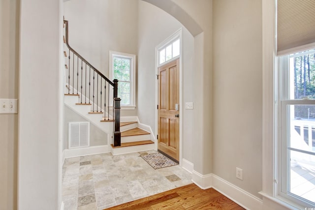 foyer entrance with arched walkways, visible vents, stairs, and baseboards