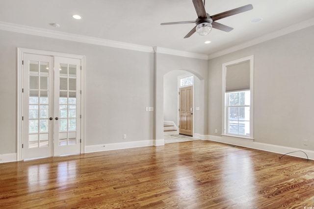 spare room featuring crown molding, baseboards, ceiling fan, wood finished floors, and arched walkways