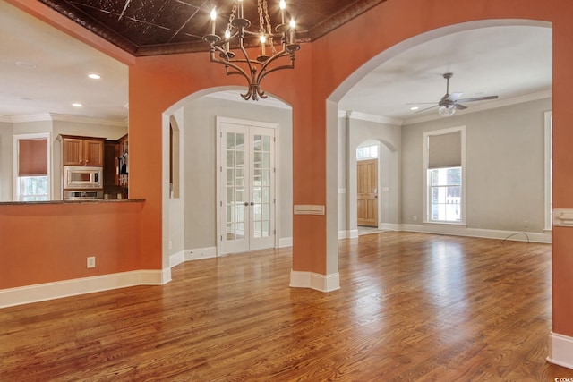 interior space with ornamental molding, ceiling fan with notable chandelier, wood finished floors, french doors, and baseboards