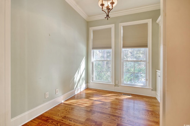 spare room featuring visible vents, baseboards, ornamental molding, wood finished floors, and a notable chandelier