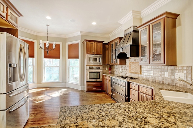 kitchen with light stone counters, appliances with stainless steel finishes, brown cabinetry, a notable chandelier, and a sink