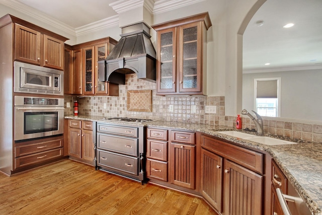 kitchen with light wood-style flooring, a sink, ornamental molding, stainless steel appliances, and custom range hood