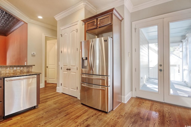 kitchen featuring dark stone countertops, appliances with stainless steel finishes, crown molding, and light wood-style floors