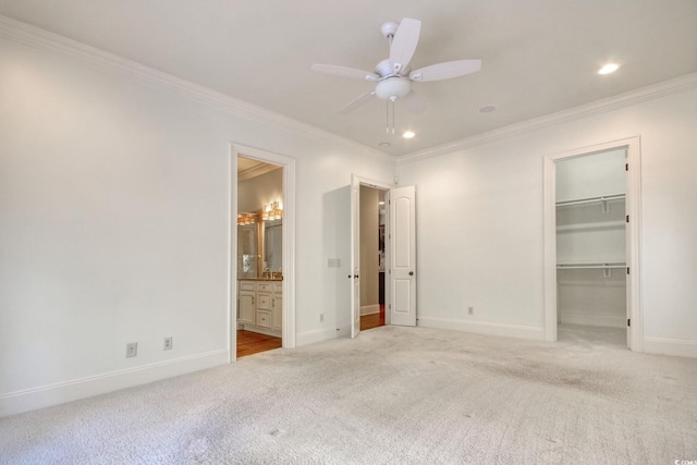 unfurnished bedroom with a walk in closet, crown molding, light colored carpet, and baseboards