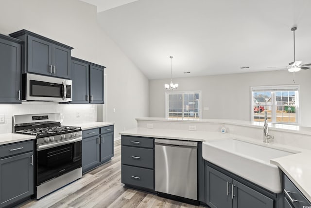 kitchen with sink, hanging light fixtures, stainless steel appliances, decorative backsplash, and ceiling fan with notable chandelier