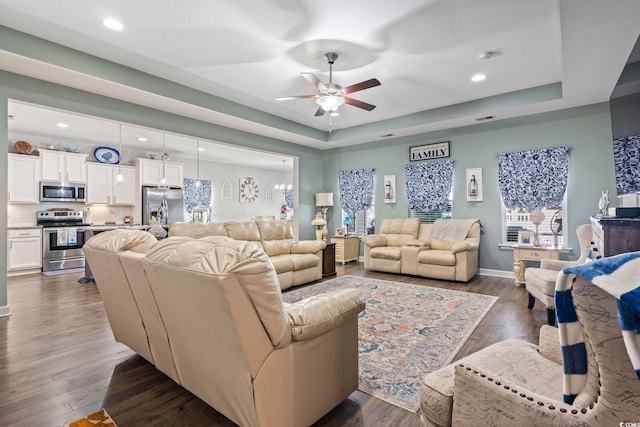 living room featuring dark wood-type flooring, ceiling fan, and a tray ceiling