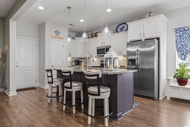 kitchen with tasteful backsplash, white cabinets, a kitchen island with sink, stainless steel appliances, and light stone countertops