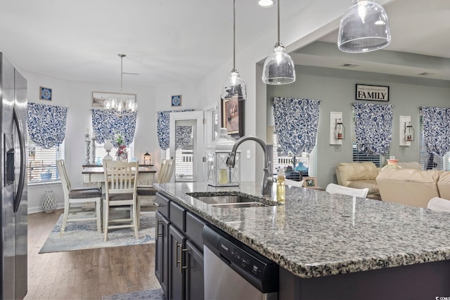 kitchen featuring stainless steel appliances, light stone countertops, sink, and a kitchen island with sink