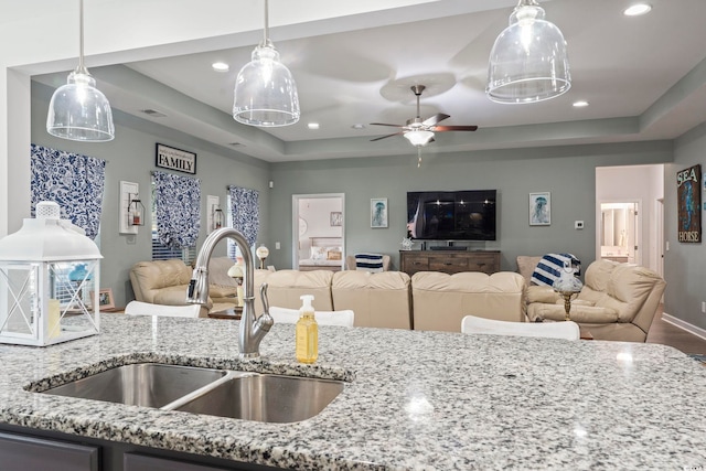 kitchen with sink, light stone counters, and a tray ceiling