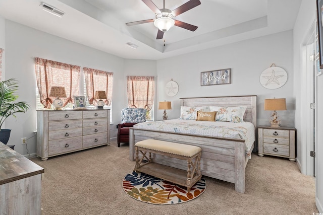 carpeted bedroom with ceiling fan and a raised ceiling