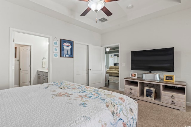 carpeted bedroom with ceiling fan, a tray ceiling, and ensuite bath