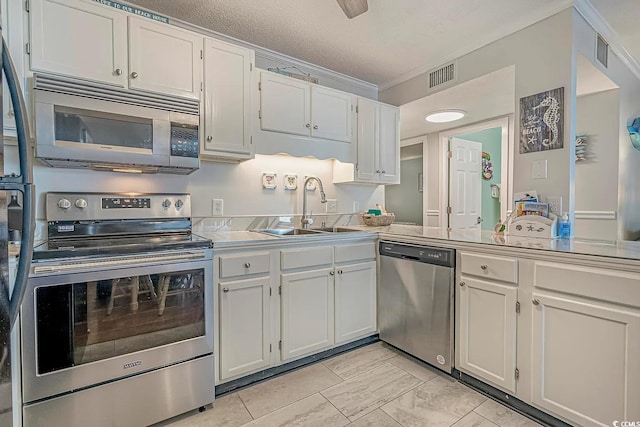 kitchen with sink, white cabinets, ornamental molding, stainless steel appliances, and a textured ceiling