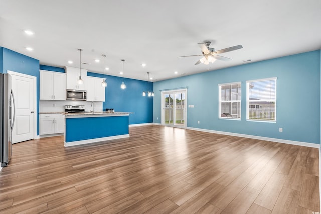 kitchen featuring hanging light fixtures, light wood-type flooring, appliances with stainless steel finishes, an island with sink, and white cabinets