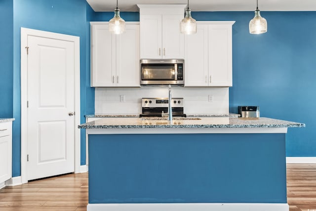 kitchen featuring appliances with stainless steel finishes, white cabinetry, sink, decorative backsplash, and a kitchen island with sink