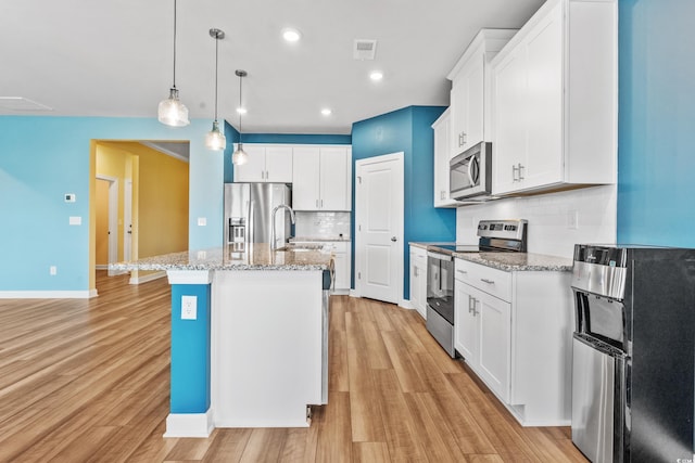 kitchen featuring decorative light fixtures, appliances with stainless steel finishes, an island with sink, white cabinets, and backsplash