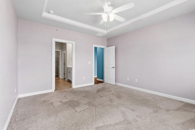 unfurnished bedroom with ensuite bathroom, ornamental molding, light colored carpet, ceiling fan, and a tray ceiling