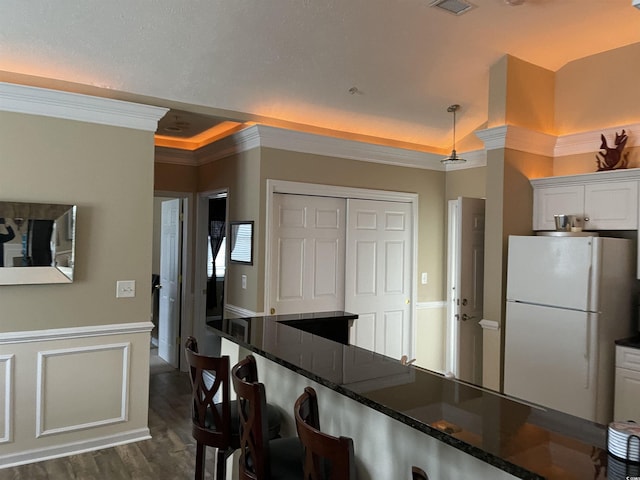 kitchen featuring white cabinetry, dark stone countertops, white refrigerator, ornamental molding, and a tray ceiling