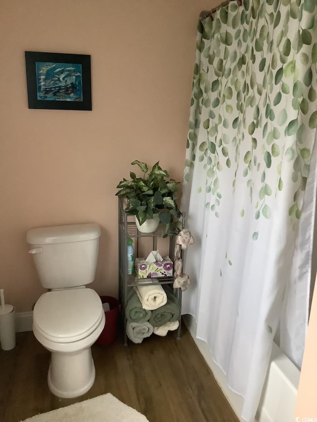 bathroom with wood-type flooring, shower / bathtub combination with curtain, and toilet