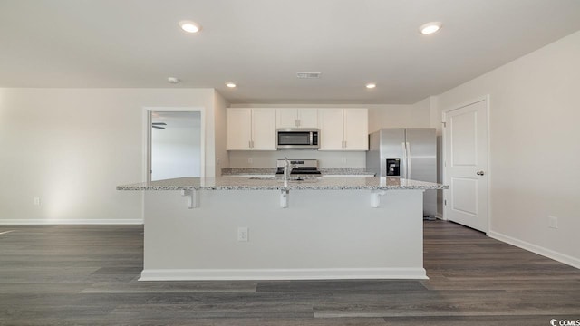 kitchen with appliances with stainless steel finishes, white cabinetry, light stone counters, an island with sink, and dark hardwood / wood-style flooring