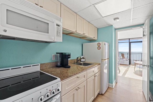 kitchen with light wood finished floors, a paneled ceiling, white cabinets, a sink, and white appliances