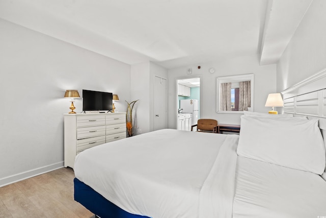 bedroom with light wood finished floors, baseboards, and freestanding refrigerator